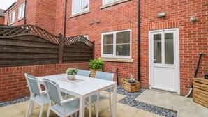 A brick house with a white door, a small patio with a table and chairs, and a wooden fence. - Valiant House (Scarborough)