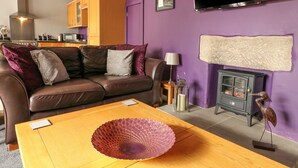 A living room with a brown leather sofa, a wooden coffee table with a decorative bowl, a television, a fireplace, and a kitchen in the background. - Royal Oak (Matlock)