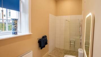 A bathroom with a window, a shower, a toilet, and a sink.