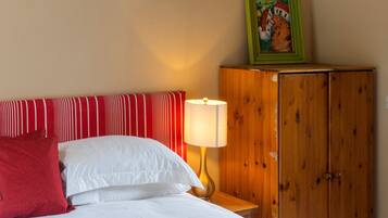 Habitación de hotel con cama, almohadas, mesita de noche con lámpara, armario de madera y un cuadro en la pared.