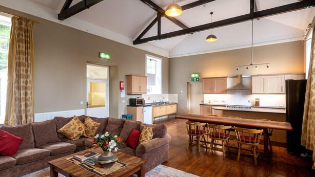 A spacious living area with a sofa set, a coffee table, and a dining table with chairs. There is a kitchen area with cabinets and appliances.