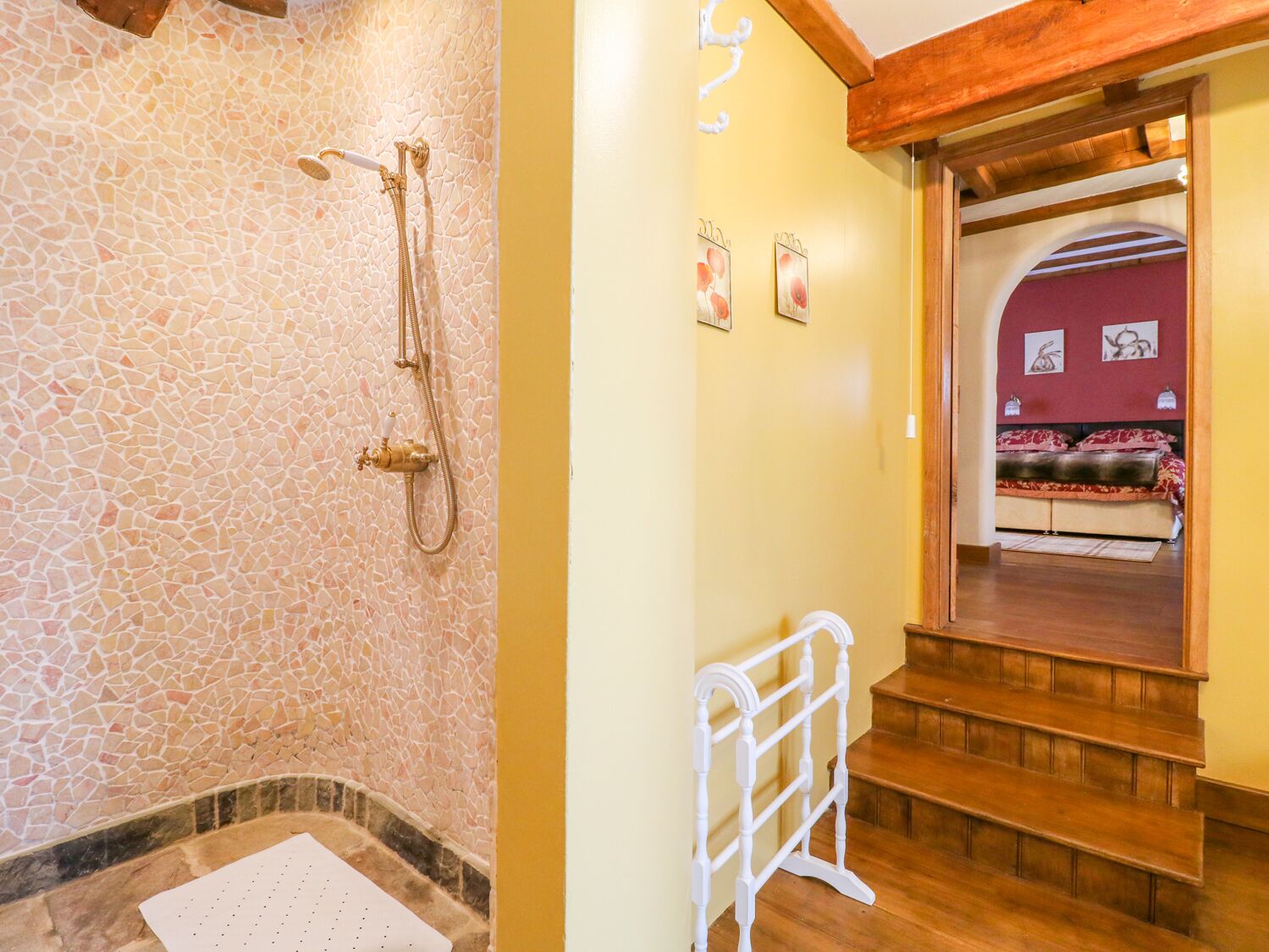 Une salle de bain avec un mur en mosaïque, une douche et un escalier en bois menant à une chambre dotée d’un mur rouge et d’un lit.