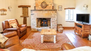 A cozy living room with a stone fireplace, leather sofa, and a television. - Woodland Lodge (Alfreton)