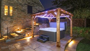 A stone building with a wooden pergola and a hot tub. - Woodland Lodge (Alfreton)