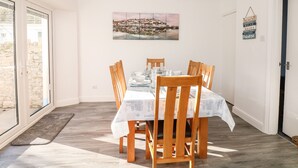 Ein Essbereich mit einem Tisch, gedeckt für sechs Personen, Holzstühlen, Blick durch eine Glastür und einem Stadtbild an der Wand.