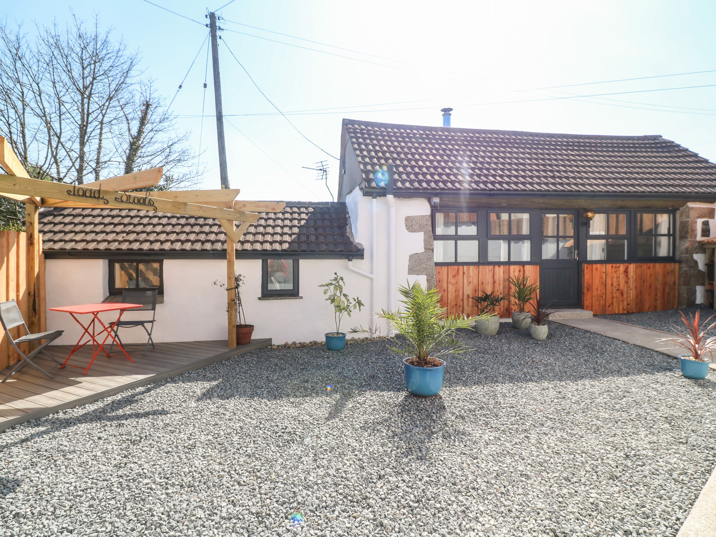 Ein Gebäude mit einem Ziegeldach, einer Holzpergola und einer Schotterterrasse mit Blumentöpfen.