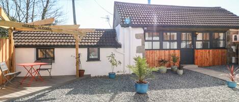 A building with a tiled roof, a wooden pergola, and a gravel patio with potted plants.