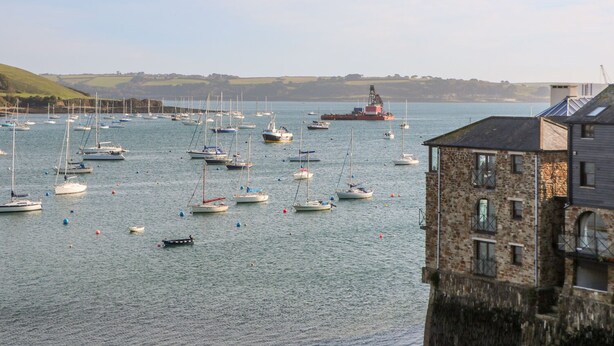 A harbor with multiple sailboats and a large ship in the background. - Toadstools (Helston)