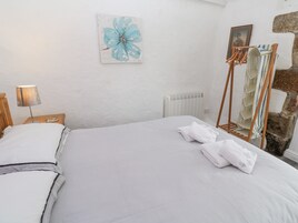 Una cama bien tendida con sábanas blancas, una lámpara de noche, una obra de arte enmarcada de una flor y un perchero con toallas dobladas.