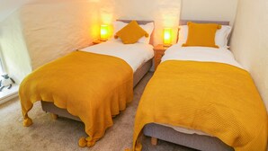 A room with two beds, each with a yellow knitted blanket and pillow, and bedside lamps. - Tilberthwaite Farm Cottage (Coniston)