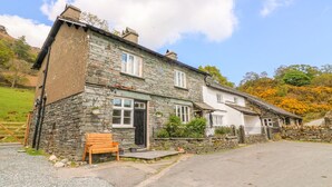 A stone house with a front door, windows, and a bench outside. - Tilberthwaite Farm Cottage (Coniston)