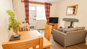 A cozy living room with a wooden dining table, a sofa, a television, and a fireplace. - Tilberthwaite Farm Cottage (Coniston)