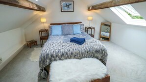 Una camera da letto con soffitto spiovente, due abat-jour, un letto con biancheria a motivi decorativi, una panca bianca e soffice e un quadro incorniciato appeso al muro.