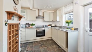 A kitchen with white cabinets, a built-in oven, a wine rack, and a window with a view. - Rigg Cottage (Whitby)