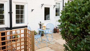 A patio with a table and chairs, a wooden fence, and potted plants. - Rigg Cottage (Whitby)