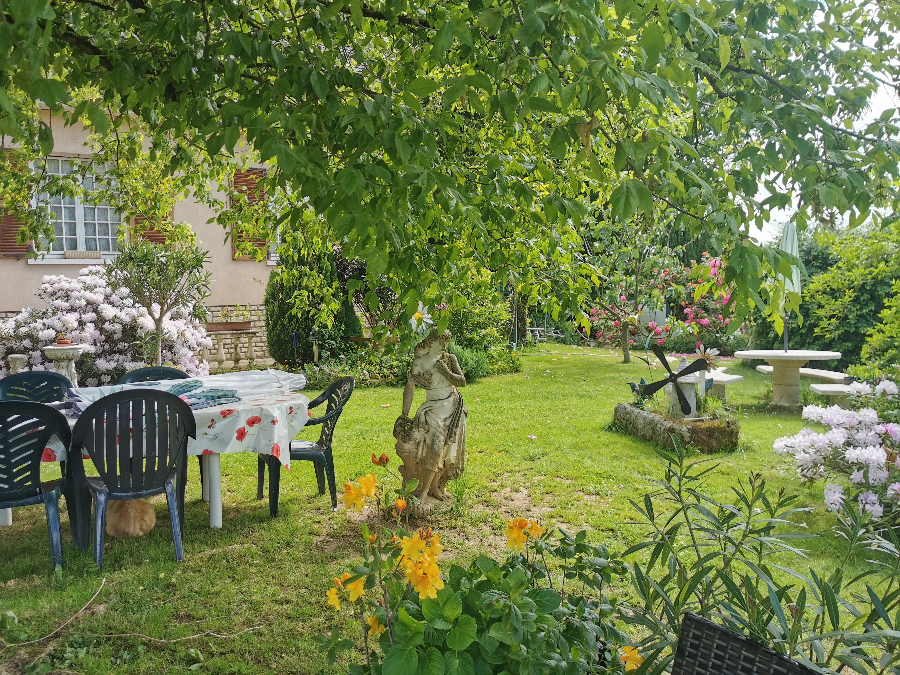 A garden with a table and chairs, a statue, and various plants and flowers.