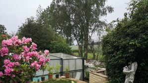 Un invernadero con techo de cristal, rodeado de un jardín con flores rosas y una estatua.