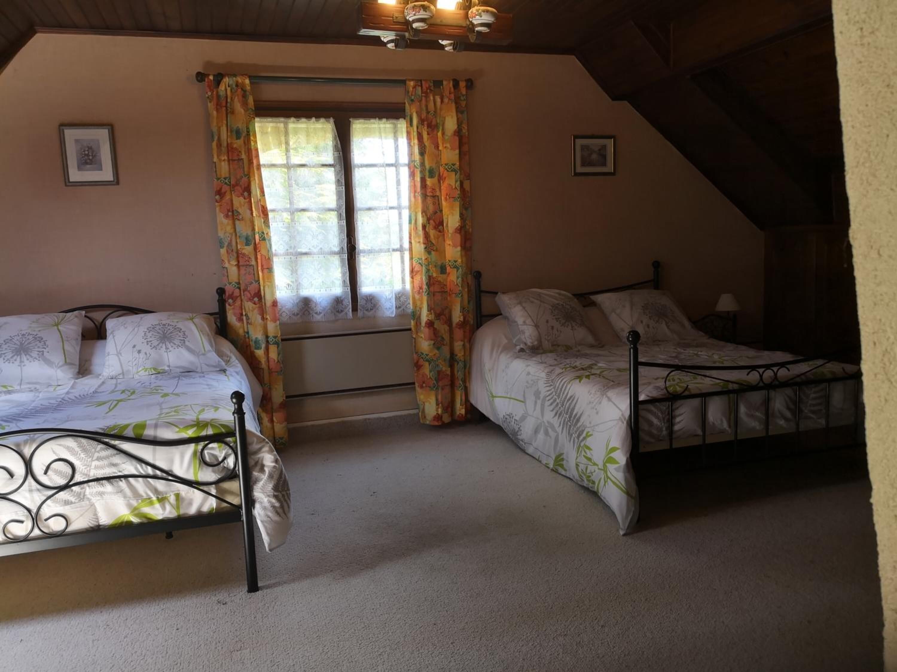 A bedroom with two beds, a window with curtains, and a ceiling fan.