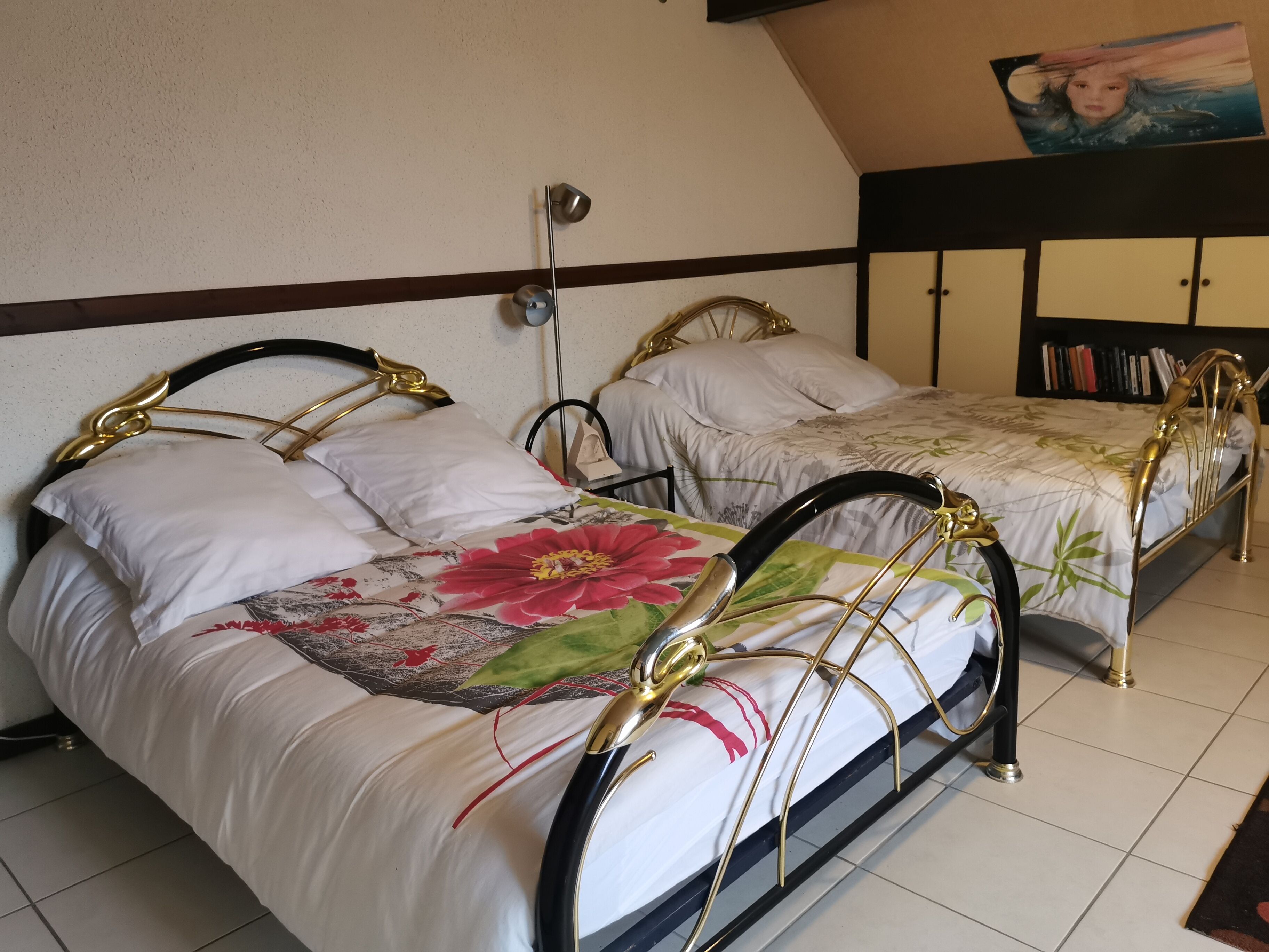Ein Schlafzimmer mit zwei Betten, jeweils mit floralem Bettbezug und goldenen Kopfteilen.
