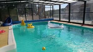 Una piscina interior con agua azul cristalina, juguetes inflables y vistas al exterior a través de amplios ventanales.