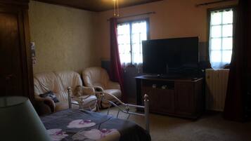 Un dormitorio con una cama, televisión, una silla y ventilador de techo.