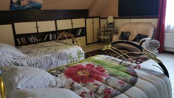 A bedroom with two beds, a bookshelf, a chair, and a TV.