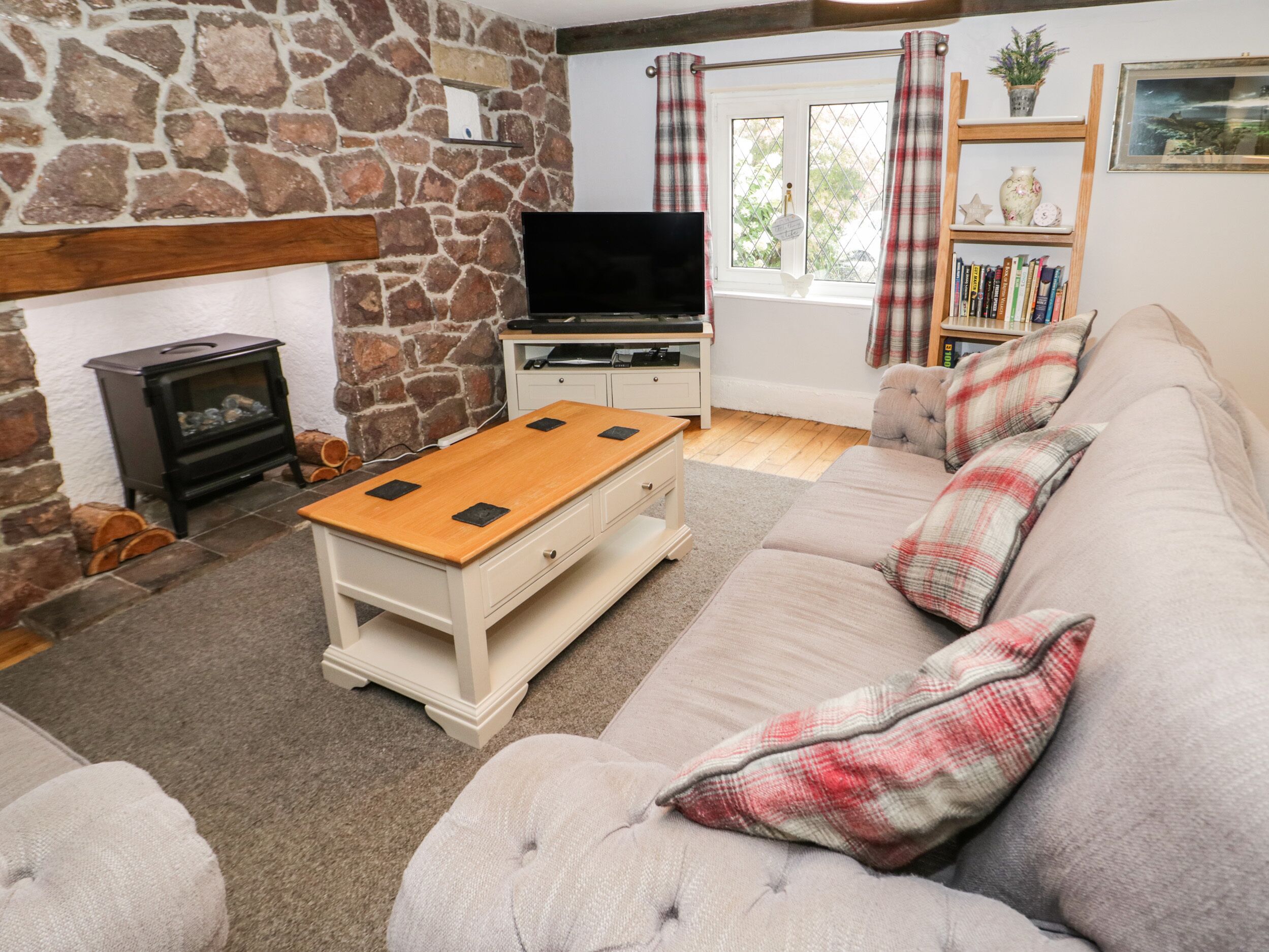 A cozy living room with a stone wall, a fireplace, a TV, a sofa, and a bookshelf.