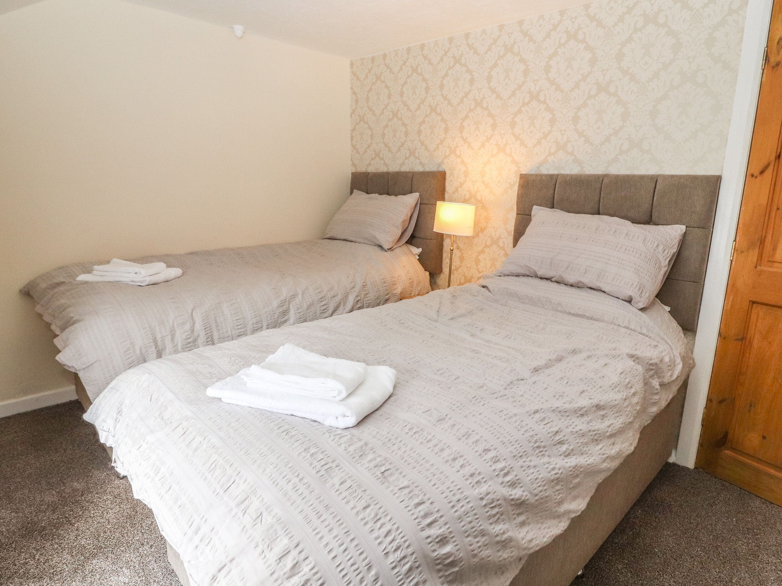 A hotel room with two beds, each with a headboard, a bedside lamp, and folded towels on the beds.