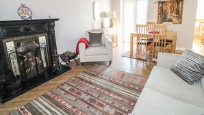 A living room with a fireplace, a sofa, a dining table with chairs, and a patterned rug. - Cranny Corner (Ballymena)