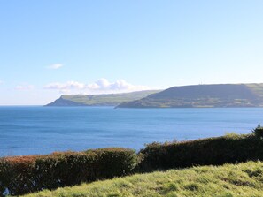 Un paysage côtier offrant une vue dégagée sur la mer, avec un premier plan herbeux et une colline surmontée d’une falaise au loin.