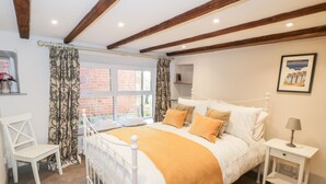 Un dormitorio con una cama blanca, un plaid amarillo y una mesita de noche blanca con una lámpara.