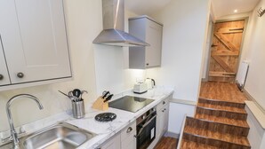 Cocina compacta con lavabo, estufa y tostadora. Una escalera de madera conduce a otra habitación.