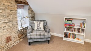 Un rincón acogedor para leer con un sillón a cuadros, una estantería llena de libros y una pared de piedra.