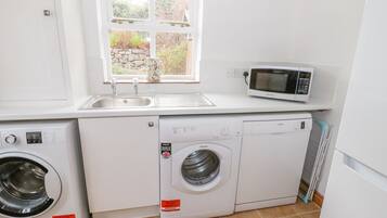 Una cocina compacta equipada con lavadora, microondas y lavabo.