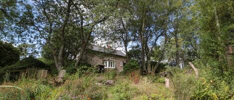 A rustic stone house surrounded by dense foliage and a variety of plants.