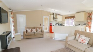 A living room with a sofa, a TV, and a fireplace. There is a kitchen area with cabinets and a microwave. - Booster's Lodge (Stratford-upon-Avon)