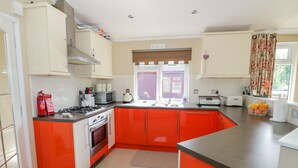 A kitchen with red cabinets, a gas stove, a microwave, and a toaster. - Booster's Lodge (Stratford-upon-Avon)