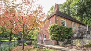 Ett traditionellt hus byggt av tegel med en stenmur och ett stort träd framför.
