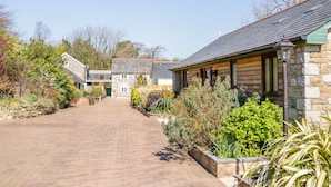 A stone building with a tiled roof, surrounded by a brick pathway and various plants. - Kingcup Cottage (St. Columb Major)