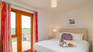 A hotel room with a bed, a tray with croissants, a cup, and a flower. - Kingcup Cottage (St. Columb Major)