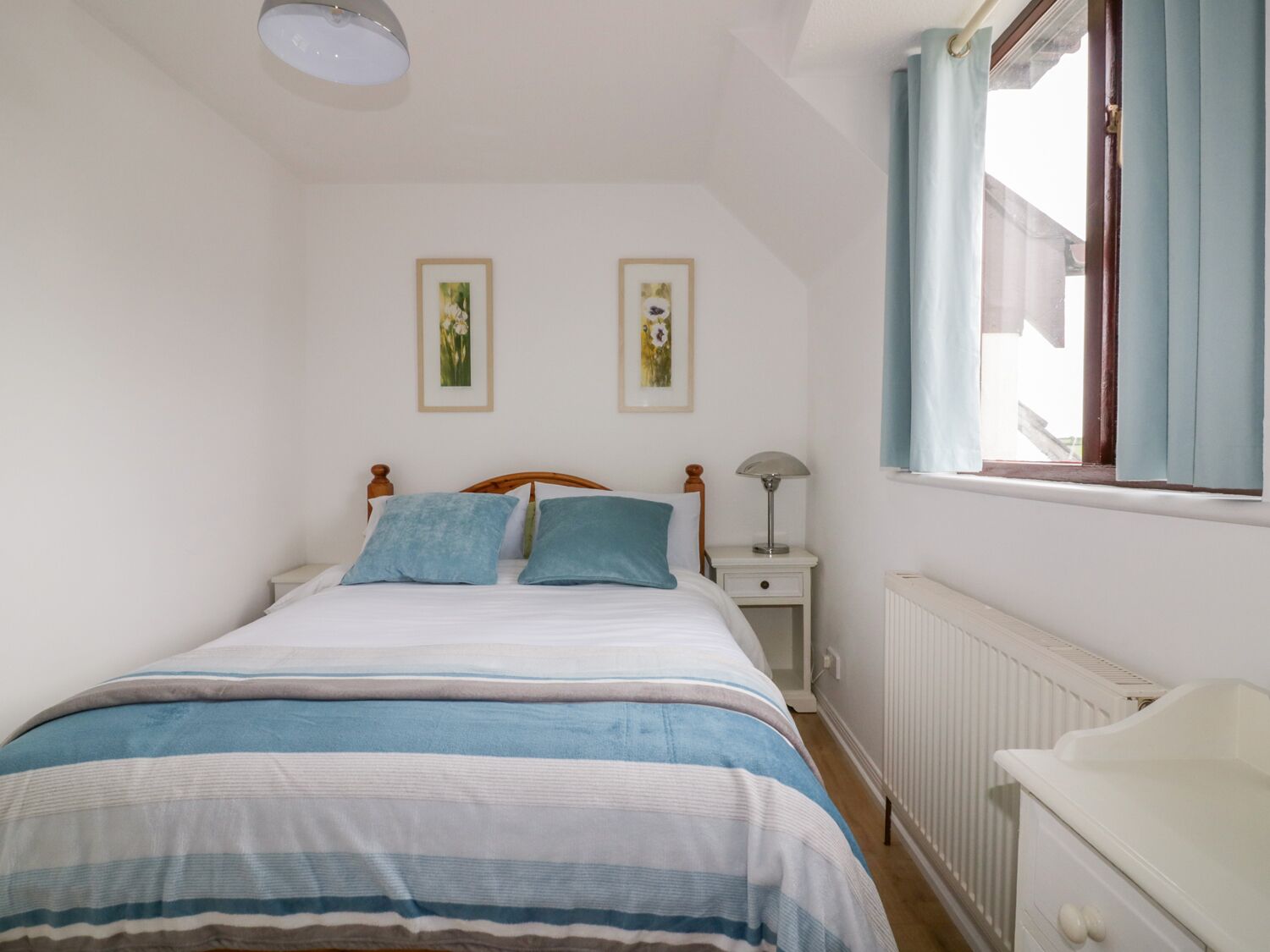 A bedroom with a bed, bedside table, lamp, window, and radiator.