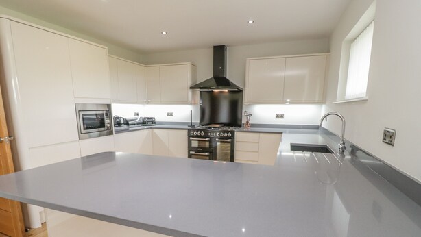 A modern kitchen with a central island, stainless steel appliances, and a black range hood. - Sannans Lodge (Llandudno)