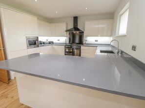A modern kitchen with a central island, stainless steel appliances, and a black range hood. - Sannans Lodge (Llandudno)