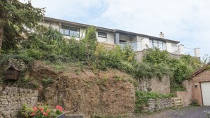A stone wall with a sign reading "SANNAS LODGE" and a small garden with pink flowers. - Sannans Lodge (Llandudno)
