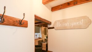 A hallway with a wooden coat rack, a sign reading "Be our guest," and a glimpse of a dining area with a table and chairs. - Milford Cottage (Belper)
