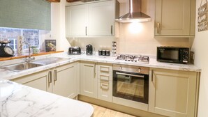 A modern kitchen with marble countertops, stainless steel appliances, and wooden beams on the ceiling. - Milford Cottage (Belper)