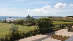 A rural landscape with a view of the sea, a castle-like structure, and a fenced property with a paved driveway. - Ocean Breeze (Marazion)