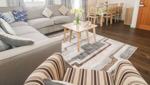 A living room with a sofa, a coffee table, and a dining area with chairs and a table. - Ocean Breeze (Marazion)