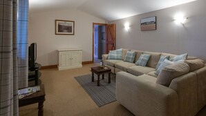 Een woonkamer met een beige bank, een houten salontafel, een televisie en een kast.