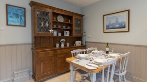 Een eetruimte met een houten kast, witte stoelen en een tafel gedekt voor vier personen.